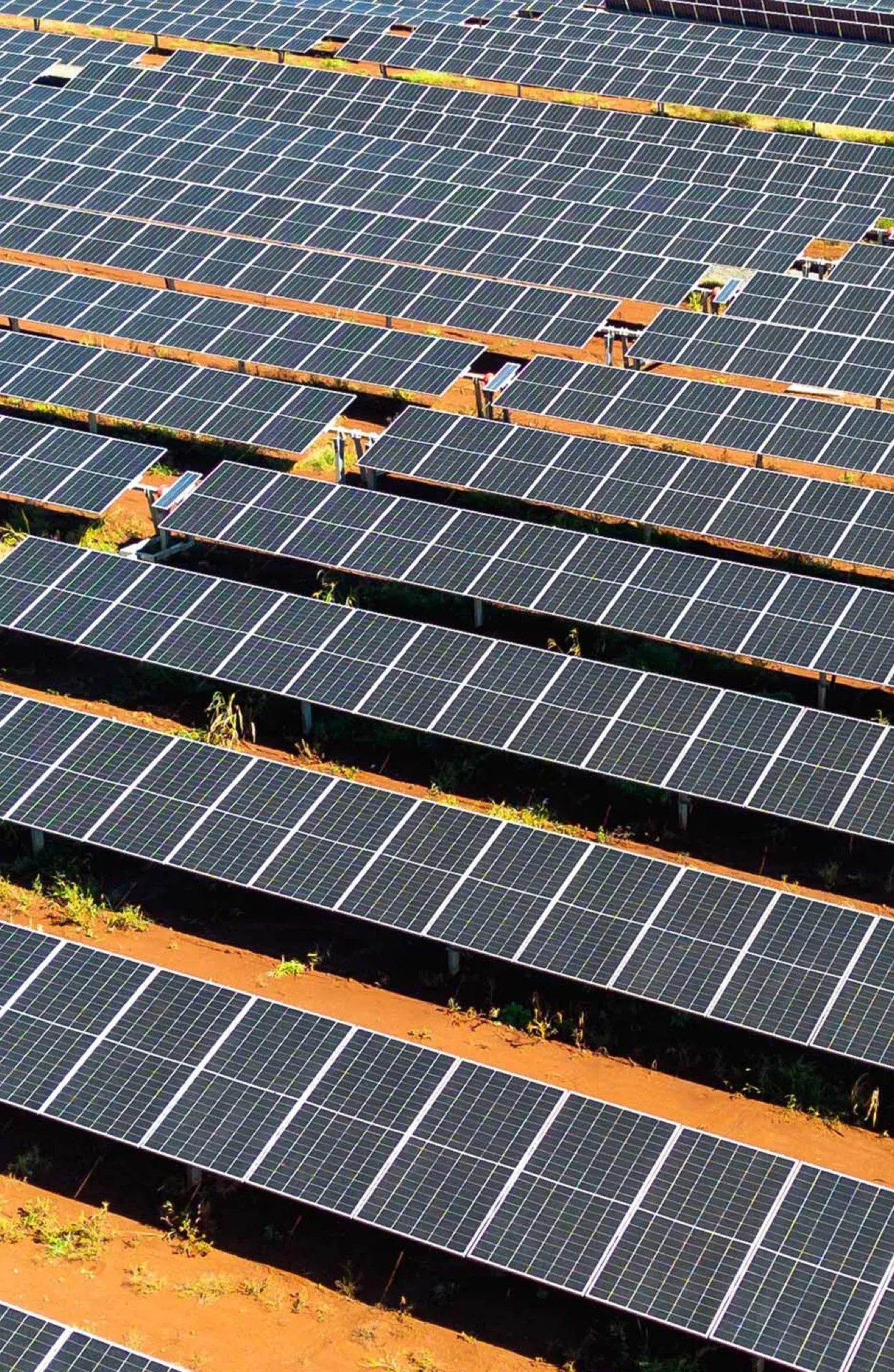 Fileiras de painéis solares sobre terra vermelha, vistas do alto, formando uma usina fotovoltaica.